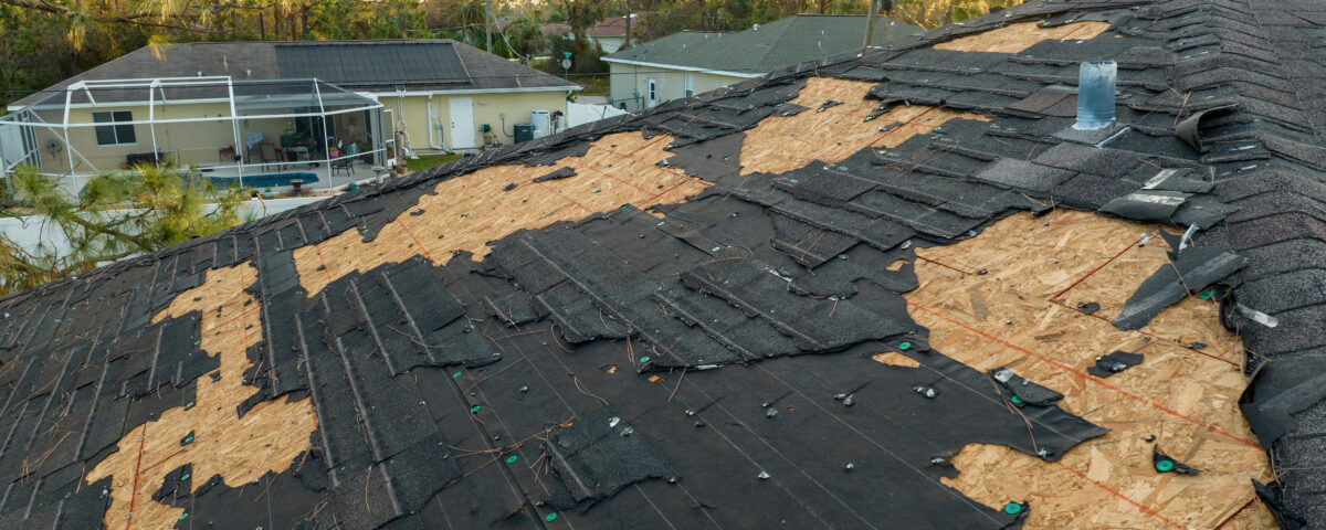 Ruined rooftop in need of repair. Wind damaged house roof with missing asphalt shingles after hurricane Ian in Florida.